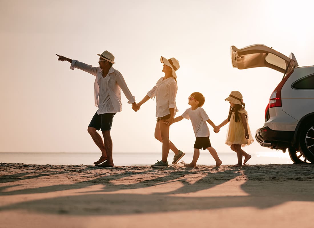 Insurance Solutions - View of a Family with Two Young Children Holding Hands and Walking on the Sand on the Beach Next to Their Car